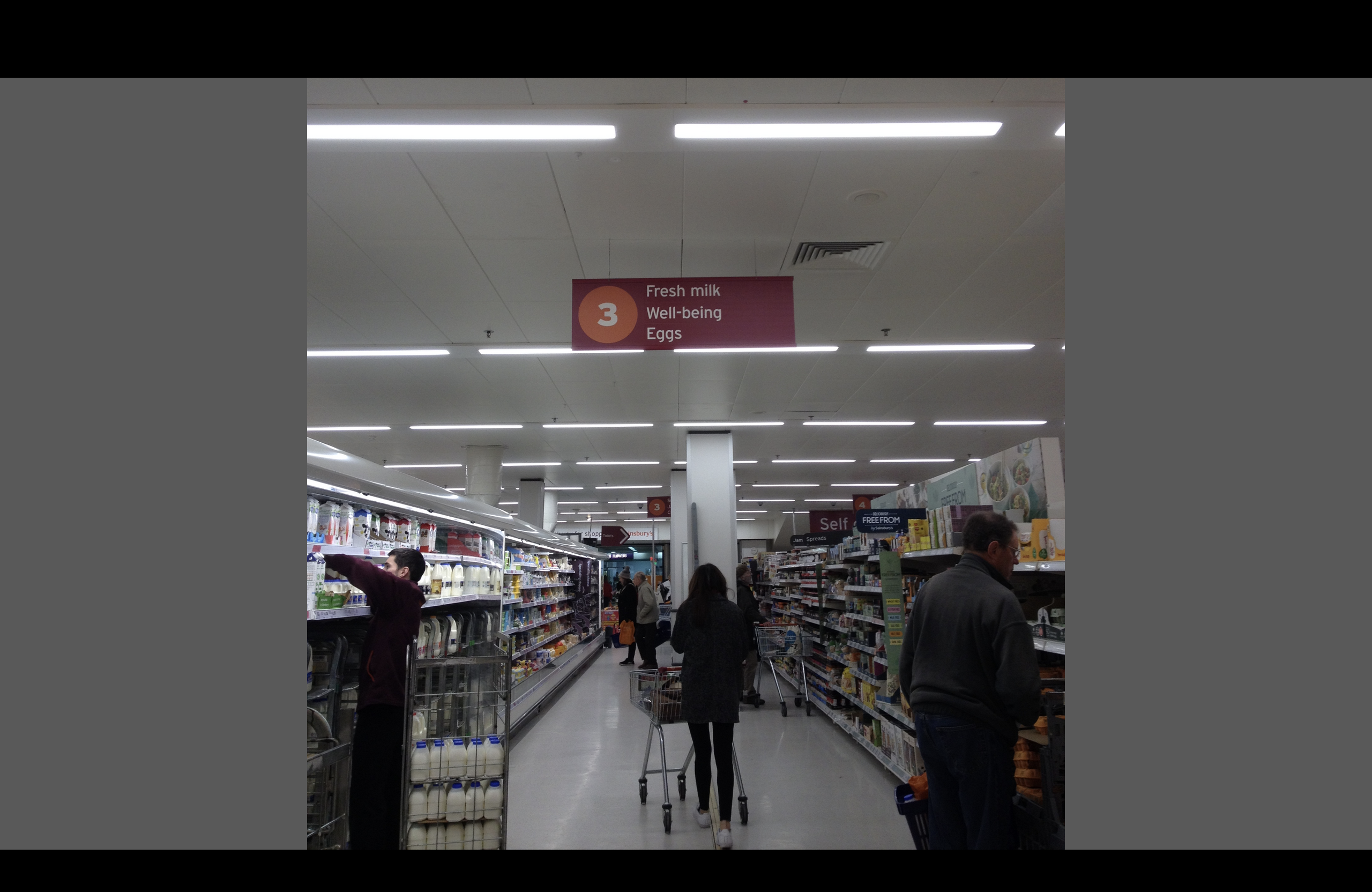 A supermarket aisle with a sign saying 'milk, wellbeing, eggs'