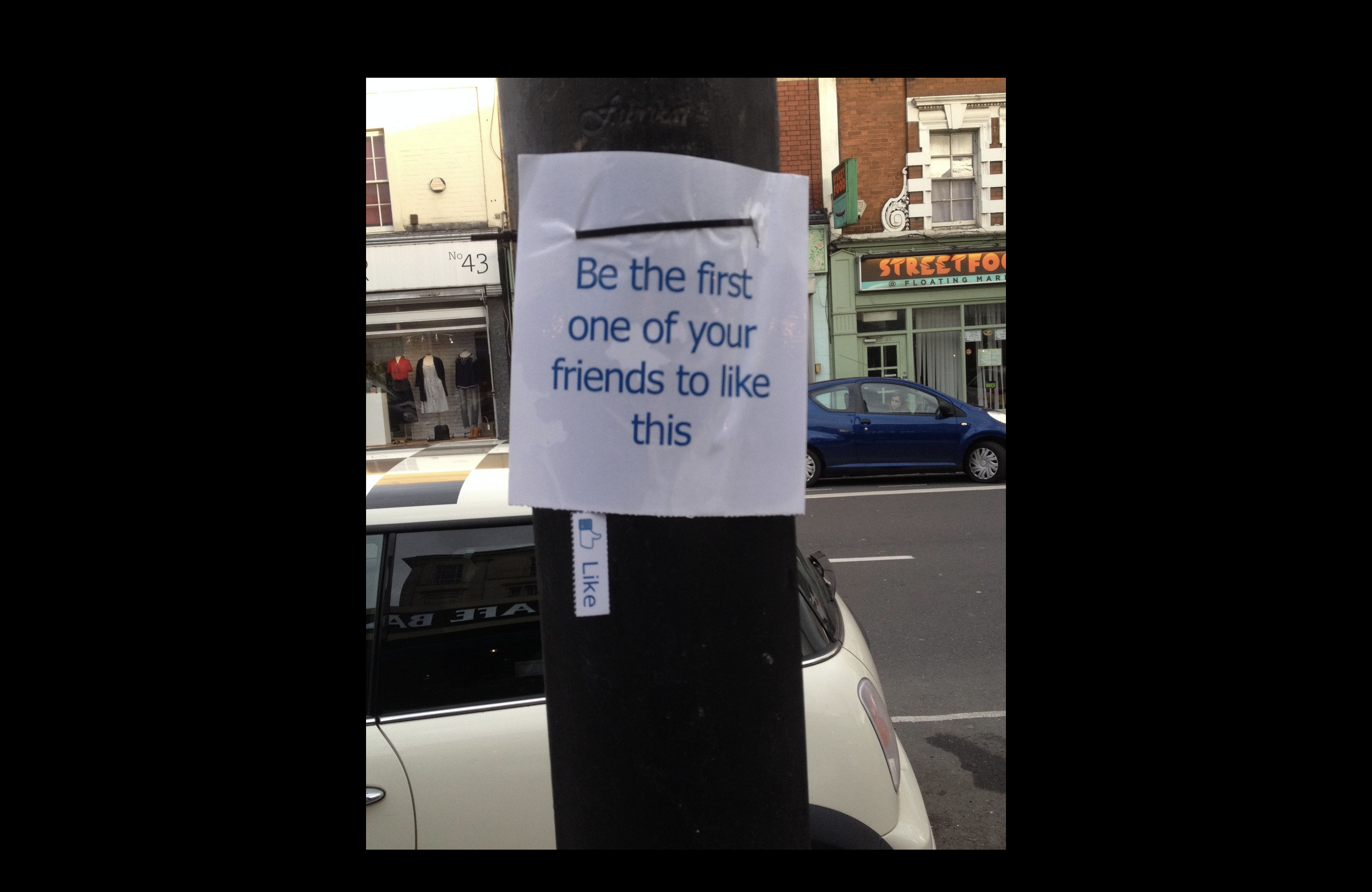A physocal paper sign on a lamppost saying 'be the first of your friends to like this' with tear-off strips